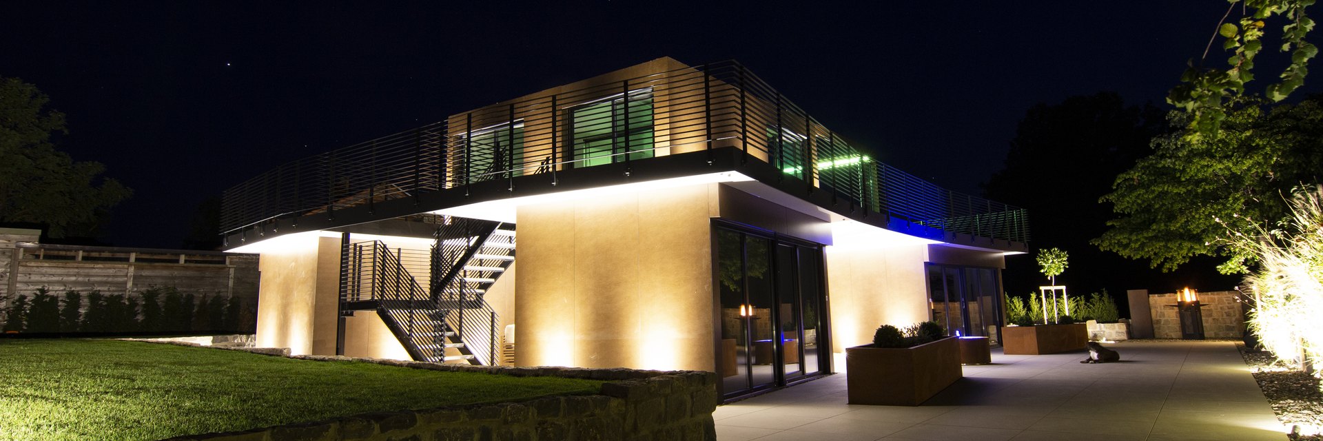 Zweigeschossiger LE Cube bei Nacht mit beleuchteter Fassade, umlaufender Dachterrasse und Au&szlig;entreppe
