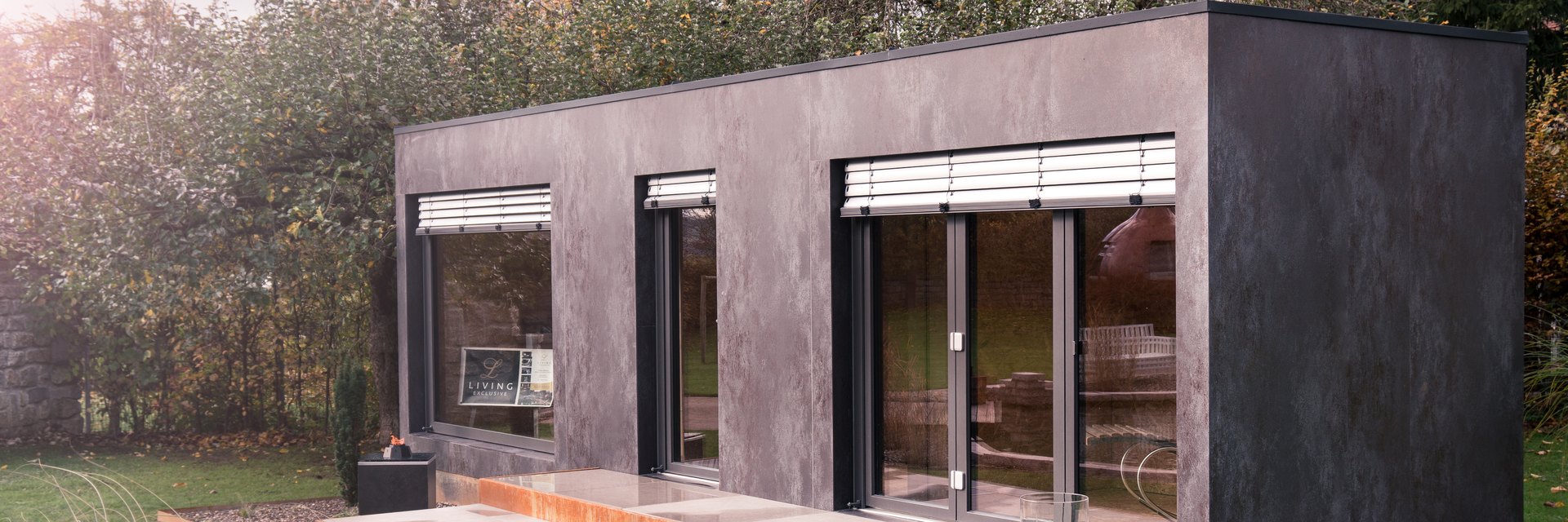 LE SpaCube im LE Showroom: ein modularer Cube in Stahlrahmenbauweise mit dunkler Fassade, Panoramafenstern und Cortenstahl-Podest, davor ein Naturpool