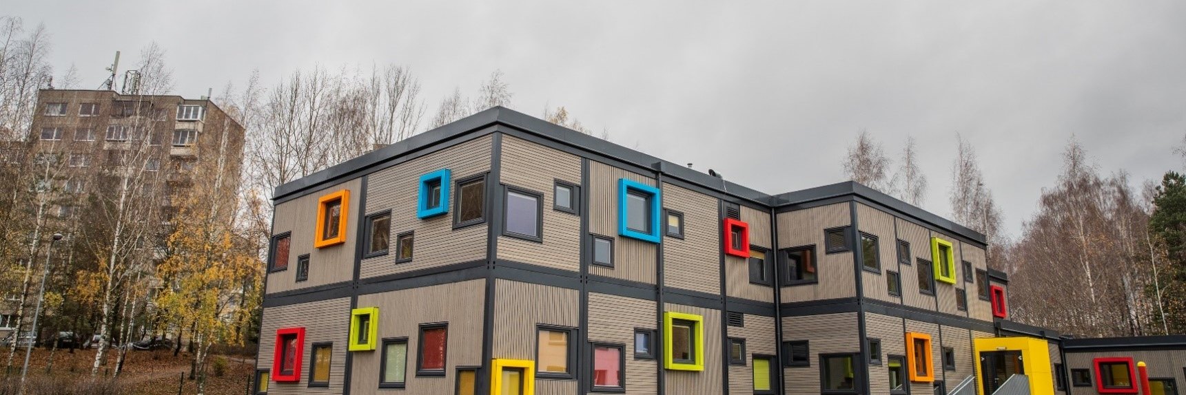 Zweigeschossiges Schul- und Kitageb&auml;ude in Modulbauweise mit bunt gerahmten Fenstern, Eckansicht