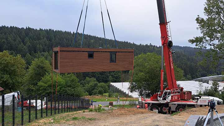 Autokran hebt ein Holzmodul &uuml;ber das vorbereitete Grundst&uuml;ck