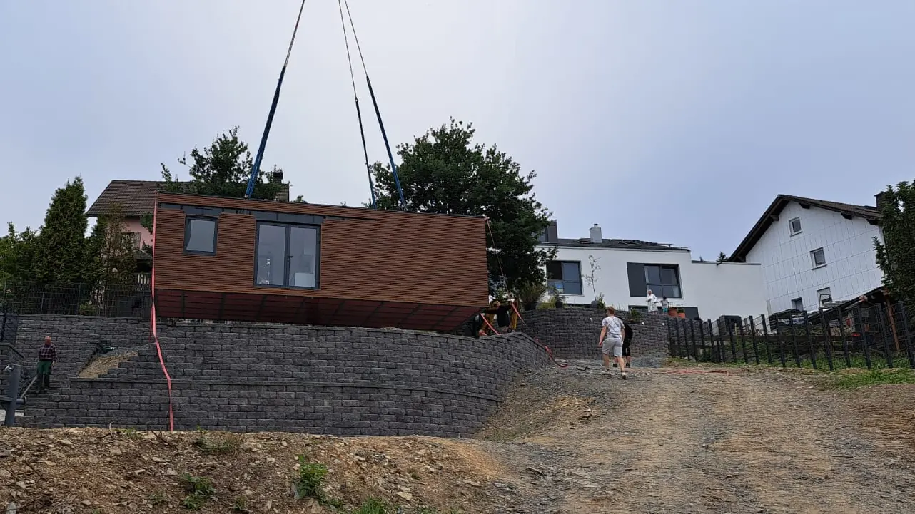 Das Wohnmodul schwebt am Kran über der Stützmauer am Hang