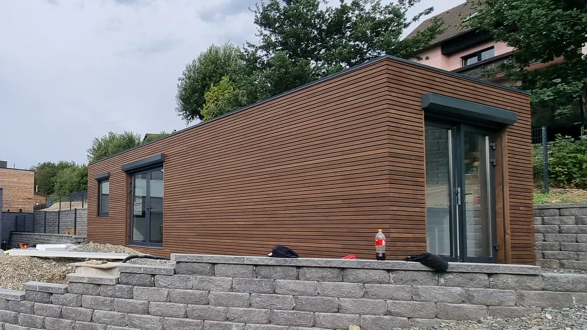 Das aufgestellte Wohnmodul oberhalb einer geschwungenen Stützmauer aus Betonsteinen