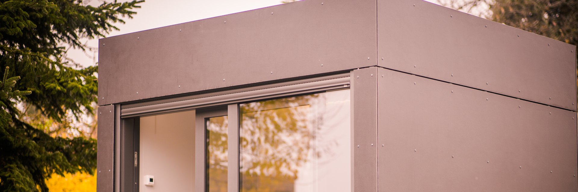 LE MiniOffice im Garten: kompakter Cube mit grauer Plattenfassade, raumhoher Schiebet&uuml;r und umlaufender Dachkante