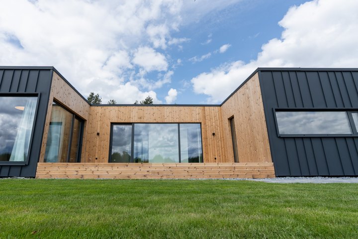 LE ModulHaus 125 m&sup2; von au&szlig;en: zwei dunkle Fl&uuml;gel mit holzverkleidetem Innenhof