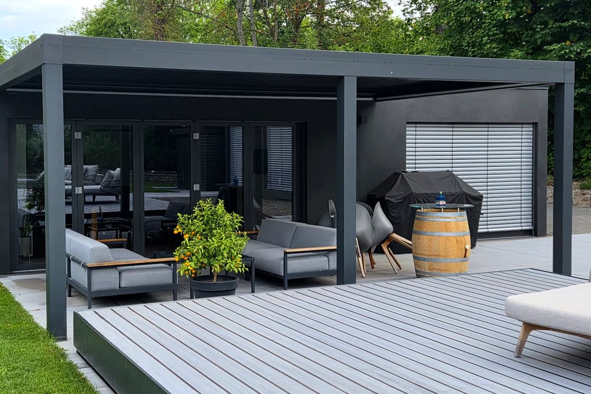 Ausgeführtes LE Poolhouse: dunkler Baukörper mit Lamellendach, Loungemöbeln und Holzdeck
