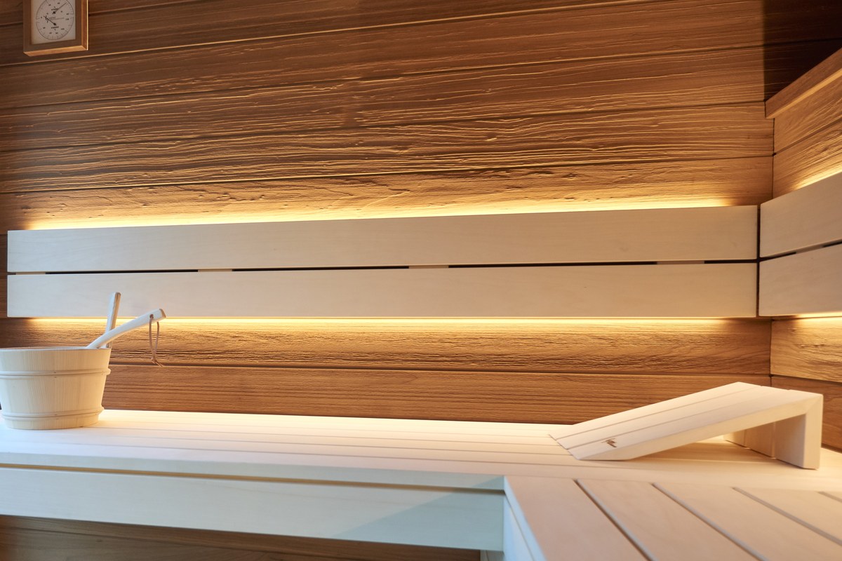Blick in die Sauna eines LE SpaCube: Bänke und Liege aus hellem Holz, indirekte Beleuchtung hinter den Rückenlehnen, Aufgusskübel mit Kelle
