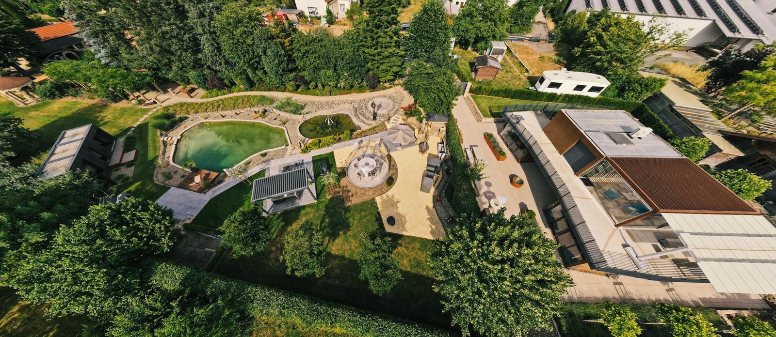Luftbild des LE Au&szlig;enshowrooms in Ebensfeld: Naturbadeteich, SkyGarden mit bepflanzten Terrassen und Sitzstufen, Pergola und Sitzgruppen sowie das Geb&auml;ude von LE Lounge und LE Cubes