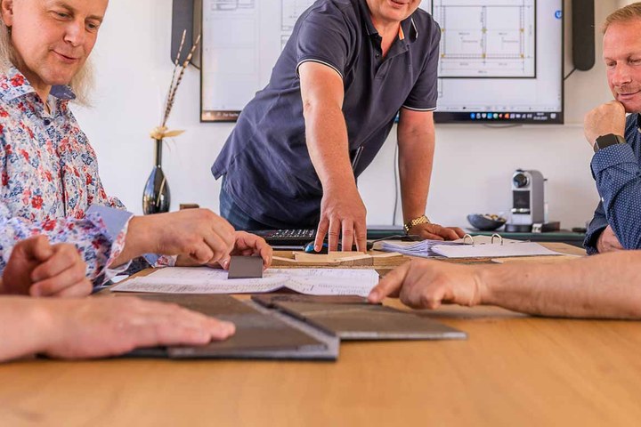 Planungsbesprechung um einen Tisch mit ausgebreiteten Plänen