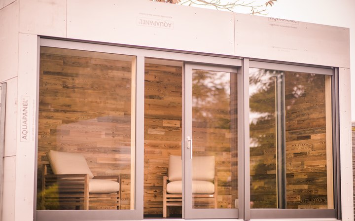 LE SaunaCube im Außenshowroom: Glasfront mit Blick auf die Altholzverkleidung, außen die bewusst sichtbar belassene AQUAPANEL-Trägerplatte