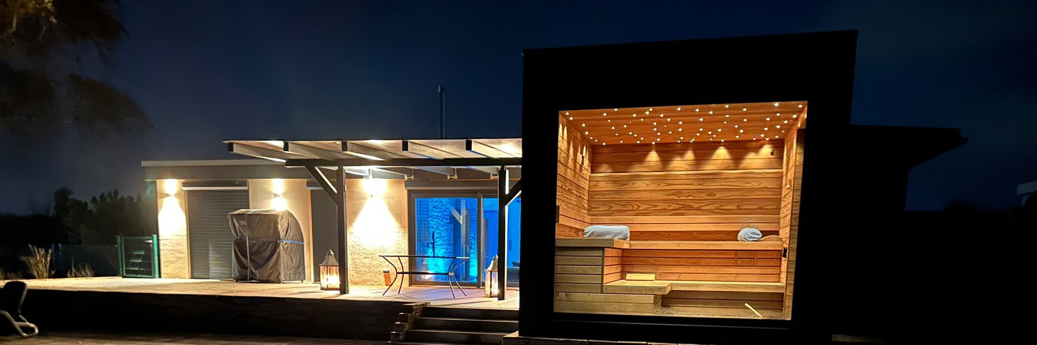 Von LE Projects geplante und gebaute Gartensauna am Abend: raumhohe Verglasung, beleuchtete Holzb&auml;nke und Sternenhimmel-Decke