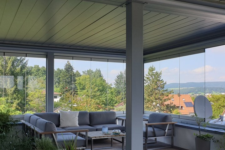 Möblierte Dachterrasse unter dem Lamellendach, ringsum rahmenlose Glasschiebeelemente