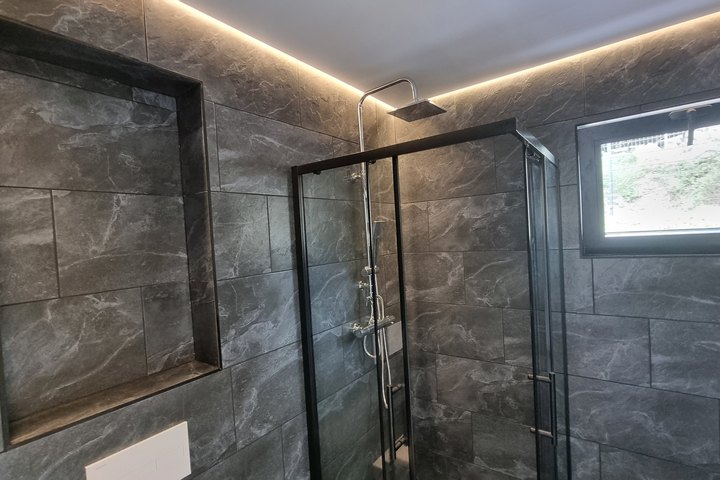 Duschbad des LE MicroHouse mit großformatigen Fliesen und Eckdusche