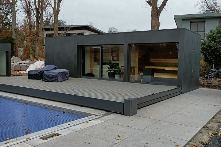 Ausgef&uuml;hrtes LE Poolhouse am Becken: dunkler Baukörper mit Holzdeck und Sauna