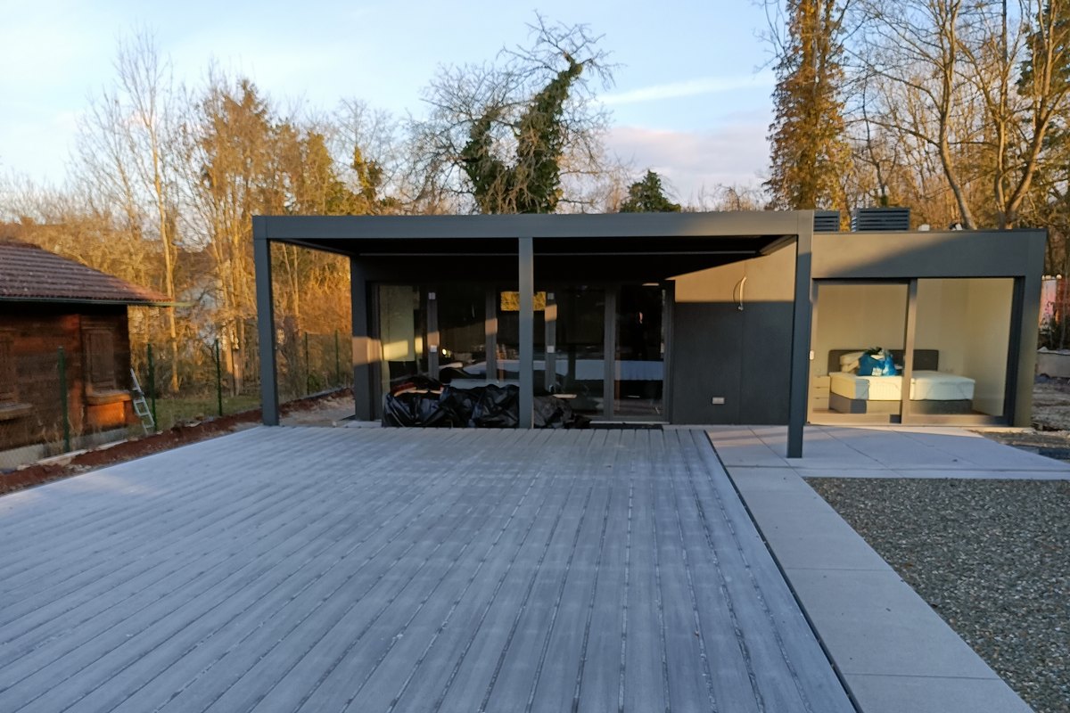 Ausgeführtes LE Poolhouse in der Abendsonne: Baukörper mit raumhoher Verglasung, davor die Lamellenpergola und die Terrasse