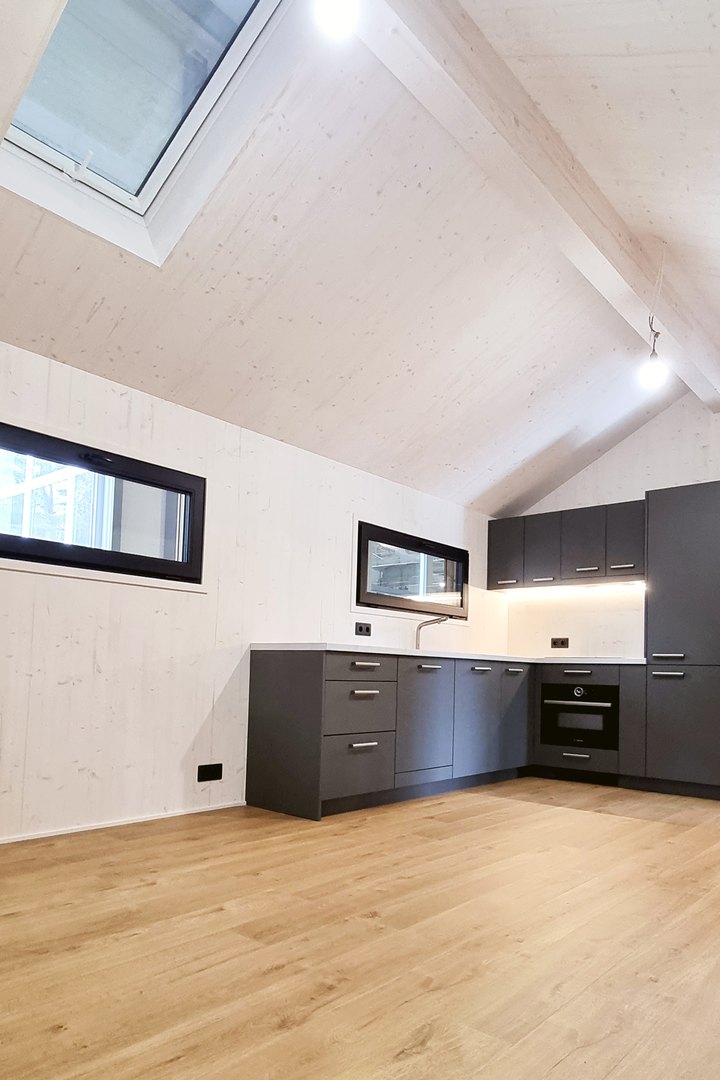 K&uuml;che eines ausgef&uuml;hrten LE TinyHouse: dunkle Einbauk&uuml;che &uuml;ber Eck unter der Dachschr&auml;ge, dar&uuml;ber Dachfenster und ein schmales Fensterband