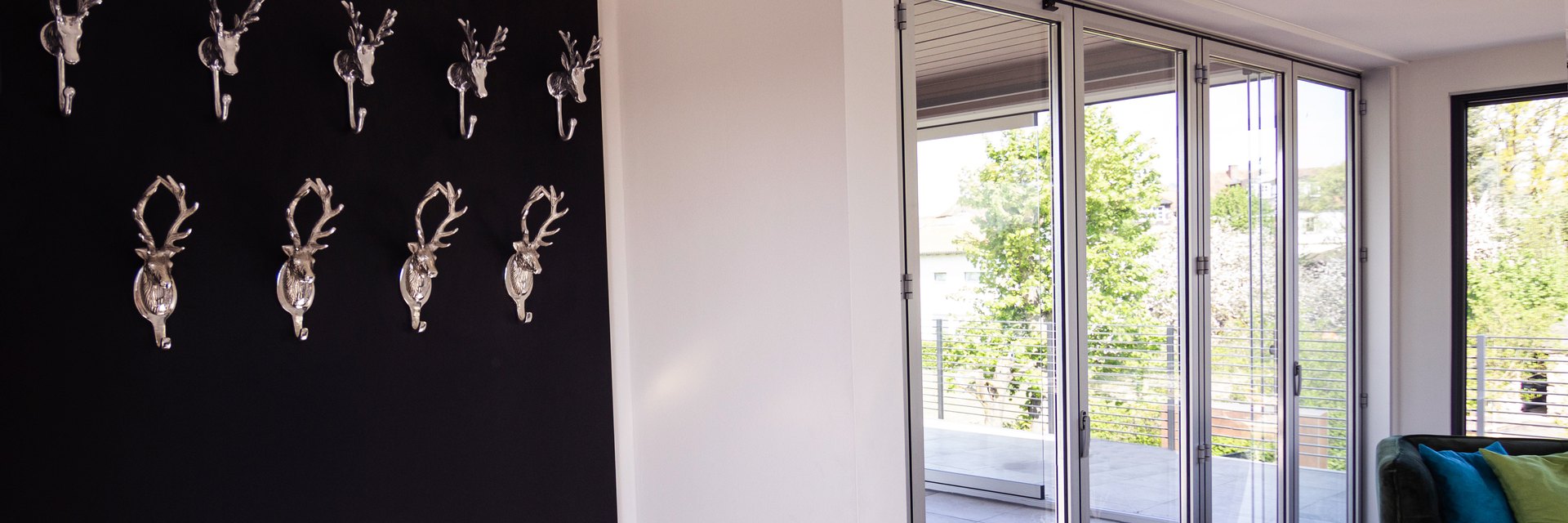Schwarzes LE Wallboard mit neun Hirschkopf-Kleiderhaken an der Wand eines hellen Eingangsbereichs mit Terrassent&uuml;r