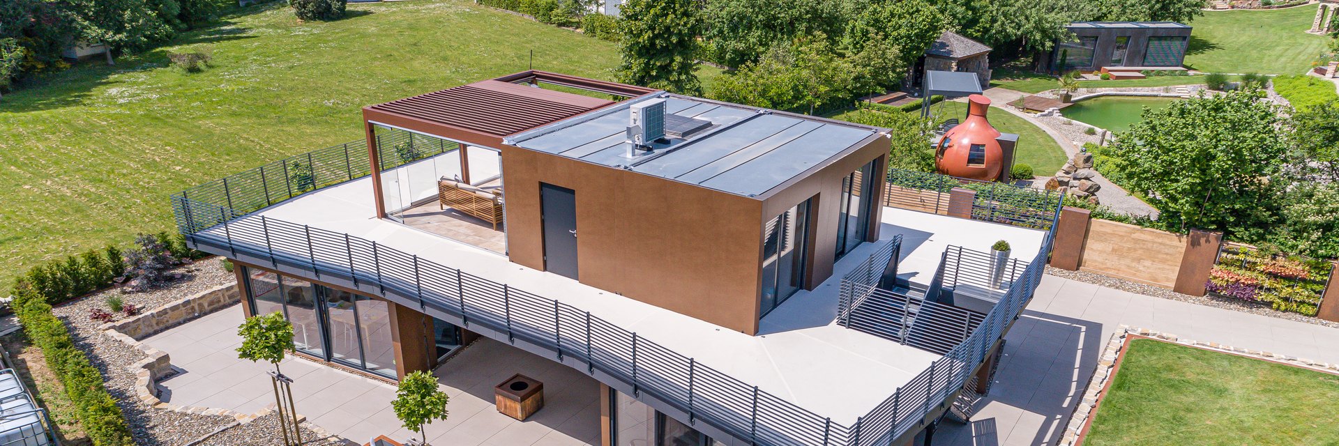Drohnenaufnahme der LE Lounge: zweigeschossiger Bauk&ouml;rper mit umlaufender Dachterrasse, Pergola und Schwimmteich aus der Vogelperspektive
