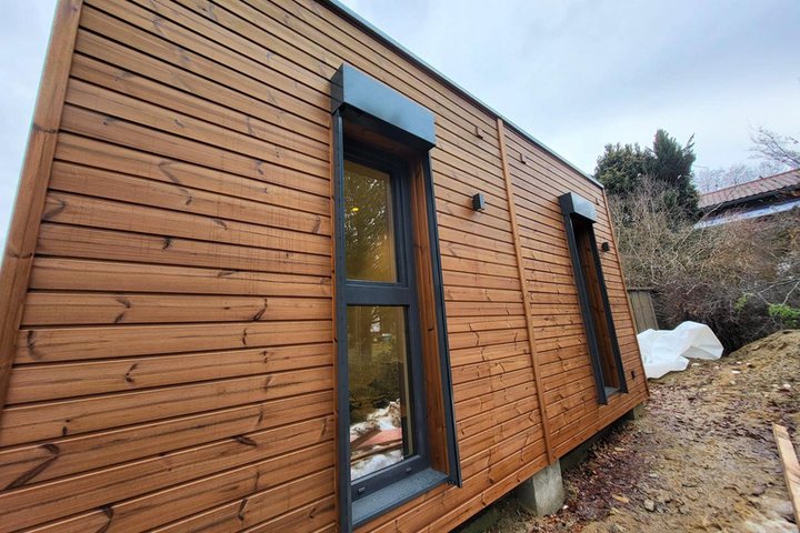 Längsseite des Wohnhauses mit horizontaler Holzfassade und hohen Fenstern