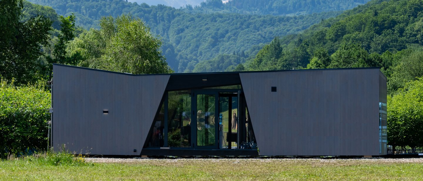 Herstellerreferenz der Palladium Corporation: Ferienhaus in Österreich vor Bergkulisse, verglaster Eingang zwischen zwei dunklen Gebäudeflügeln