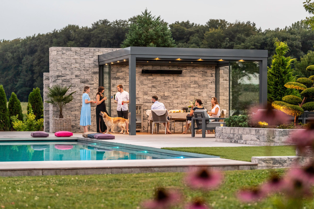 Glashaus vor einer Natursteinwand am Pool, Menschen und ein Hund auf der Terrasse