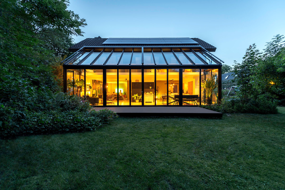 Beleuchteter Wintergarten mit Glasdach in einem Garten in der Abenddämmerung