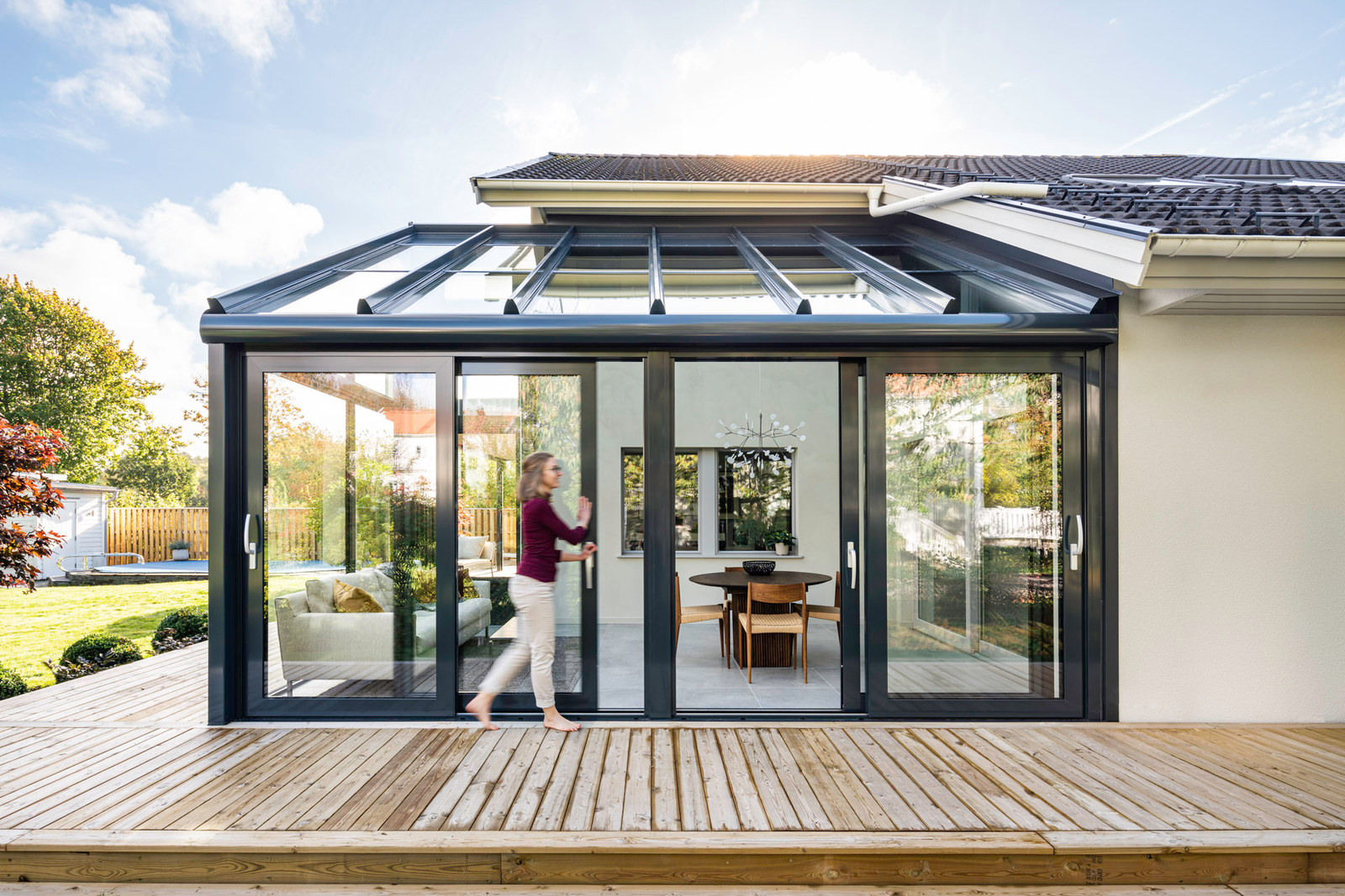 Wintergarten mit Glasdach und raumhohen Glasfronten an einem hellen Einfamilienhaus, davor eine Holzterrasse